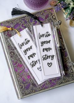 two bookmarks that say write your own story and have tassels attached to them