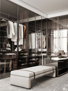 a walk in closet with a bench and clothes on hangers next to glass doors