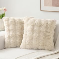 two white pillows sitting on top of a couch next to a vase with tulips