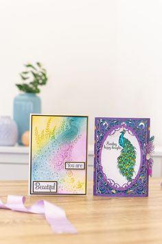 two cards on a table, one with a peacock and the other with a rainbow background