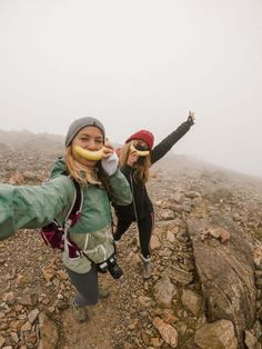 two young women standing on top of a rocky mountain eating an apple and posing for the camera