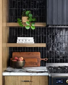 a kitchen with black tiled walls and wooden shelves above the stove top, along with a bowl of fruit on a cutting board