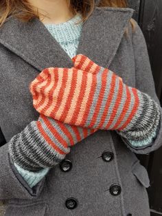 a close up of a person wearing a gray coat and orange striped mittens