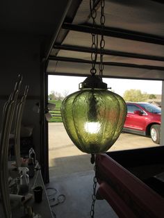 a green glass light hanging from a ceiling in a garage next to a red car