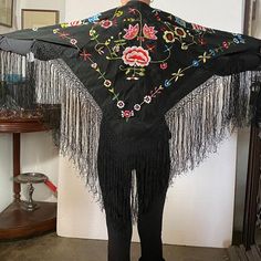 DETAILS A small, vintage traditional Flamenco dancer's black shawl or mantoncillo pico with a floral embroidery design and long fringe.  COLOR(S) Multi-color on black ground  PLACE OF ORIGIN Spain | Europe  DATE 20th century  DIMENSIONS Width 63 Depth 63 inches Without fringe: Width 36 Depth 36 inches Traditional Black Shawl With Floral Embroidery, Black Bohemian Shawl For Spring, Black Embroidered Bohemian Shawl, Traditional Black Embroidered Shawl, Black Embroidered Shawl With Traditional Drape, Traditional Embroidered Shawl For Spring, Black Fringed Shawl For Festival, Black Folk Style Shawl For Festival, Black Bohemian Shawl With Embroidered Border