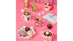 a pink table topped with two mugs filled with hot chocolate and marshmallows