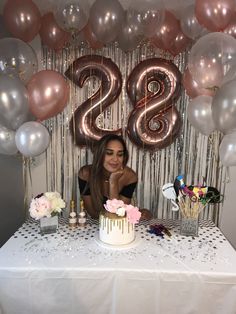 a woman sitting at a table with a cake and balloons