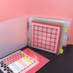 a binder and some papers sitting on a table next to each other with pink walls in the background