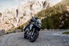 a black motorcycle parked on top of a cobblestone road in front of mountains