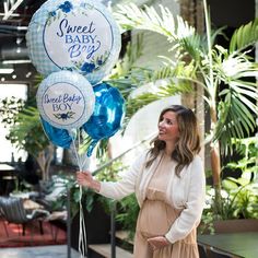 a woman holding some blue and white balloons that say sweet baby boy on one side