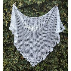 a white crocheted shawl hanging on a bushy wall covered in ivy