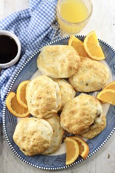 biscuits and orange slices on a plate next to a cup of coffee with a blue checkered napkin