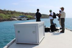 three men standing on the back of a boat with luggage and water in the background