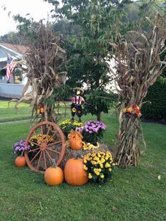 an arrangement of pumpkins and flowers on the grass in front of a house with a wagon