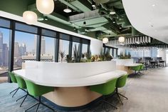 an office with green and white chairs and plants on the desks in front of large windows