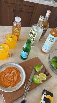 a table topped with bottles and glasses filled with alcohol next to a cutting board full of limes