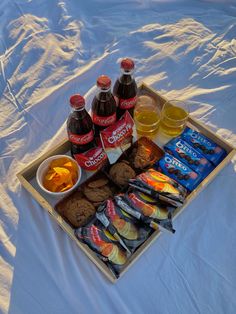 a tray filled with snacks and drinks on top of a white sheet covered tablecloth