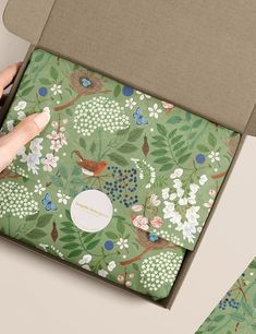 a person is opening a box with a green floral pattern on it and there are two other boxes in front of the box