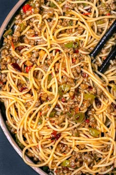 a pan filled with noodles and meat on top of a blue tablecloth next to a pair of black chopsticks