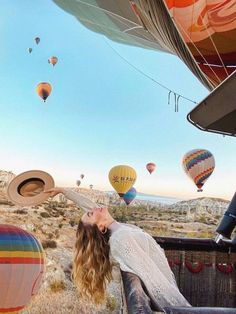 a woman is sitting in the back of a truck with hot air balloons flying above her