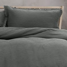 a bed with grey sheets and pillows on it