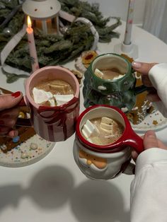 two people holding mugs of hot chocolate and marshmallows on a table