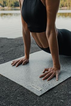 a woman is doing yoga on a mat by the water with her hands behind her head