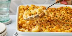 a person scooping macaroni and cheese from a casserole dish