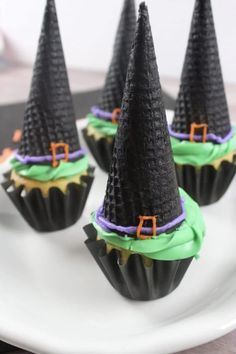 four cupcakes with green frosting and black cones on top, sitting on a white plate