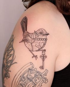 a woman's arm with a bird and key tattoo on the back of her shoulder