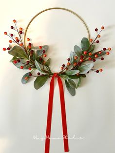 a wreath with red berries and greenery is hanging on the wall next to a ribbon