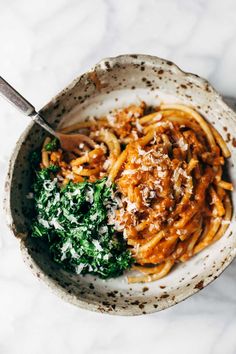 a white bowl filled with pasta and spinach on top of a marble countertop