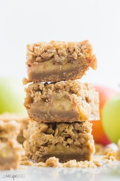 three pieces of apple pie bars stacked on top of each other with apples in the background