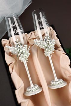 two wine glasses with flowers and pearls on them sitting in a black box next to a white veil