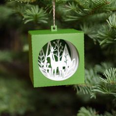 a green ornament hanging from a christmas tree with white deer and trees in the background