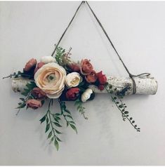 an arrangement of flowers is hanging on a white wall with a wooden stick attached to it