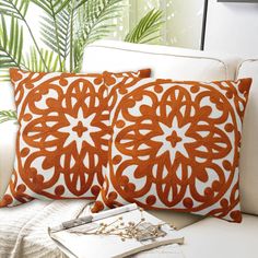 two orange and white pillows sitting on top of a couch next to a plant in a vase