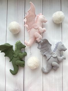 three felt dragon figurines sitting next to pom poms on a white wooden surface