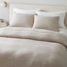 a bed with white linens and pillows in a neutral colored bedroom, along with an alarm clock on the wall