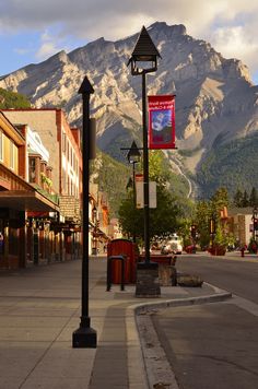 an empty street with mountains in the background and buildings on both sides that are lined with shops