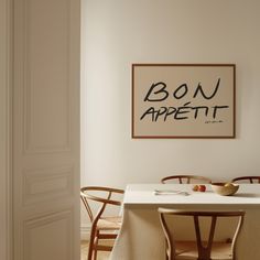 a dining room table with two chairs and a bowl of fruit on it in front of a sign that reads bon appetit