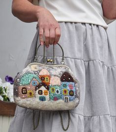 a woman is holding a purse with houses on the front and sides, while wearing white pants