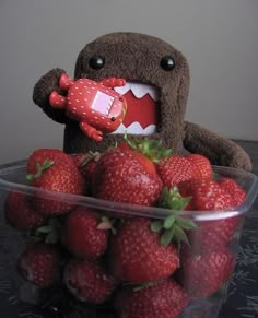 a stuffed animal holding a red object in front of a bowl full of strawberries