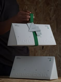 two white boxes with green ribbons tied to each other on top of one another in front of a wooden wall