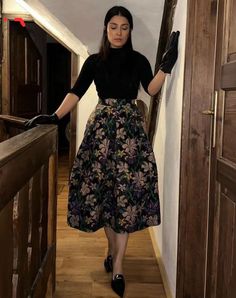 a woman is walking down the stairs in a black top and floral skirt