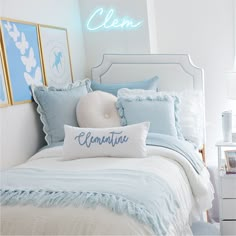 a white bed topped with pillows and blankets next to a wall mounted neon sign that reads clean