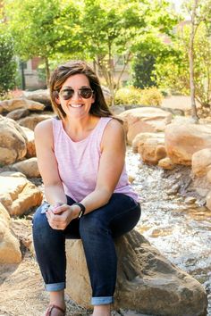 a woman sitting on top of a rock next to a river