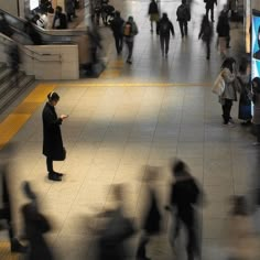 many people are walking around in the subway station and one person is using his cell phone