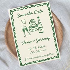 save the date card on a wooden plate with wine glasses and cake in it, surrounded by greenery