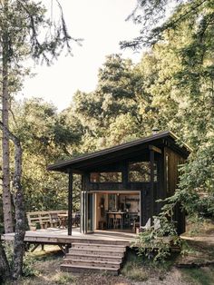 a small cabin in the woods with stairs leading up to it's patio area